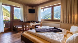 A bedroom with a wooden ceiling, a bed with white bedding, a bedside table, a chair, and a window with a mountain view. - Group house with garden close to ski resort (Finkenberg)