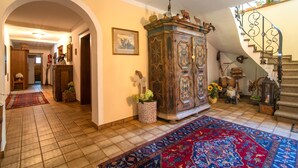Un hall d’entrée spacieux, agrémenté d’une grande armoire en bois, d’un tapis rouge à motifs et d’un escalier avec une rampe en fer forgé.