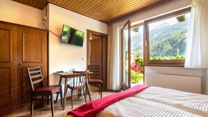 Une chambre avec un lit, un bureau et des chaises, un téléviseur fixé au mur et une fenêtre donnant sur la montagne.