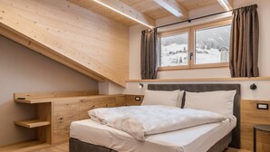 A bedroom with a bed, wooden headboard, built-in shelving, a window with curtains, and a view of a snowy landscape.
