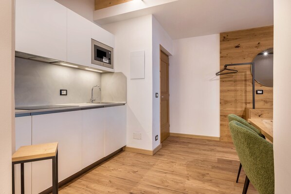 Una cocina moderna con armarios blancos, microondas integrado y una zona de comedor de madera con una silla verde.