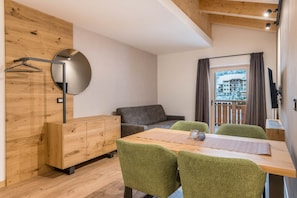 Een moderne kamer met een houten kast, een ronde spiegel, een grijze bank, een houten eettafel met stoelen en uitzicht op een gebouw door een raam met gordijnen.