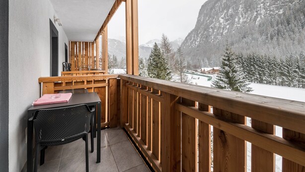 Un balcon avec une balustrade en bois, une table avec une chaise, et une vue sur des montagnes enneigées.