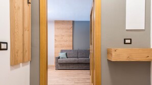 Un couloir avec une porte en bois, un canapé gris avec un coussin bleu et une étagère en bois.