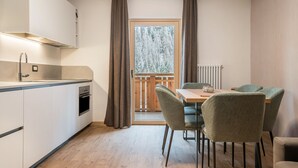 Une cuisine moderne dotée d’un four encastré, un coin repas avec une table et des chaises, et une vue sur l’extérieur à travers une fenêtre agrémentée de rideaux.