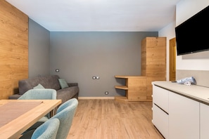 Un espacio habitable compacto con sofá, una mesa de comedor, un televisor montado en la pared y un mueble de madera.