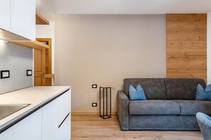 Eine moderne Küche mit weißen Schränken, einem grauen Sofa mit blauen Kissen und einer Wand in Holzoptik.