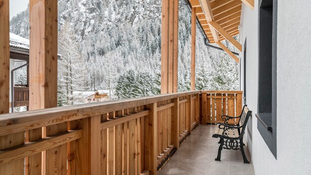 Un balcon en bois avec un banc, donnant sur une forêt enneigée.
