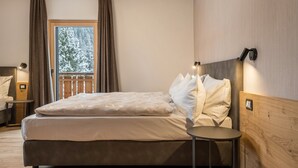 Une chambre à coucher comprenant un lit, une table de chevet, une commode, une fenêtre avec des rideaux et un luminaire fixé au mur.