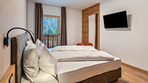 Ein Schlafzimmer mit einem Bett, einem an der Wand montierten Fernseher, einem Fenster mit Vorhängen und einem Holzboden.