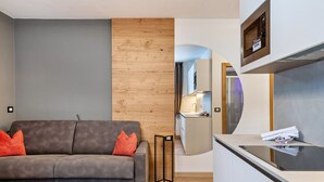 Ein modernes Wohnzimmer mit grauem Sofa, einer Holz-Akzentwand und einer Küchenzeile mit Einbauofen.