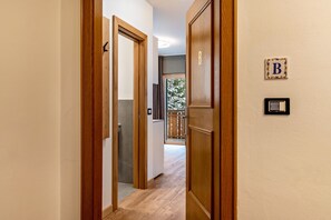 Un pasillo con puertas de madera, un interruptor de luz en la pared y una letra 'B' enmarcada en la pared.