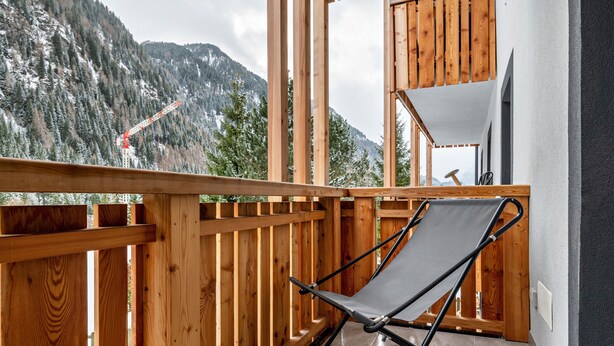 Ein Balkon mit Holzwertung, einem grauen Hängesessel und Blick auf einen verschneiten Berg.