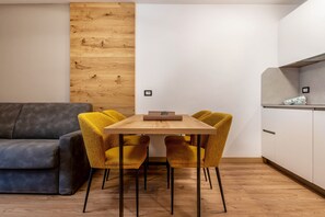 Una sala de estar moderna con una pared de acento de madera, un sofá gris y una mesa de comedor de madera con cuatro sillas amarillas.