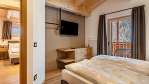 A bedroom with a bed, a TV mounted on the wall, a wooden desk, and a window with curtains. - Kamerloy Apartments - F with Mountain View, Wi-Fi, Balcony and Garden (Campitello di Fassa)