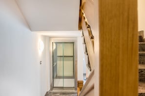 Un intérieur moderne avec un ascenseur en verre, un escalier en bois et un mur blanc et épuré.