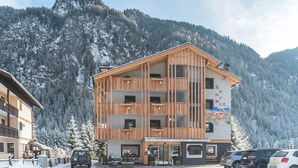 A multi-story hotel with a wooden facade, balconies, and a mountain backdrop. - Kamerloy Apartments - F with Mountain View, Wi-Fi, Balcony and Garden (Campitello di Fassa)