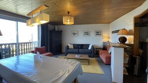 A cozy living room with a wooden ceiling, a dining table, a sofa, and a small kitchen area. - Résidence de l'Oisans 4 rooms - Quartier Cognet (Alpe d'Huez)