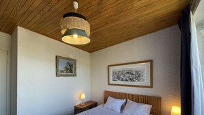 A hotel room with a large bed, two bedside tables with lamps, a wooden ceiling, and two framed pictures on the walls. - Résidence de l'Oisans 4 rooms - Quartier Cognet (Alpe d'Huez)