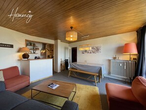 A modern hotel room with a wooden ceiling, a dining area, a bed, and a reception desk.