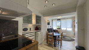 A compact kitchen with a microwave, stove, and cabinets, a dining area with a table and chairs, and a view of the outdoors through a window. - ASH - Cosy studio - La Menandière (Alpe d'Huez)