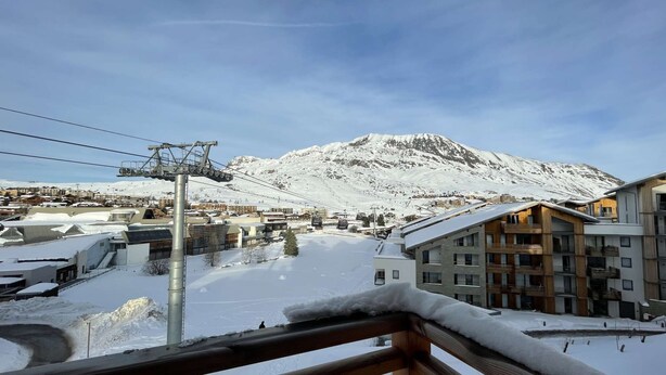 Ein verschneiter Gebirgsort mit Seilbahn, Häusern mit Balkonen und freier Bergkulisse.
