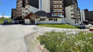 Ein mehrstöckiges Hotel mit modernem architektonischen Design, mit Balkonen und einem im Hintergrund sichtbaren Skilift.