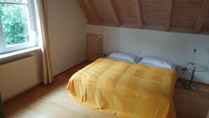 A bedroom with a large bed, a small table, and a window with curtains. - Vacation apartment for 3 on a hillside with a dream view of the lake (Öhningen)