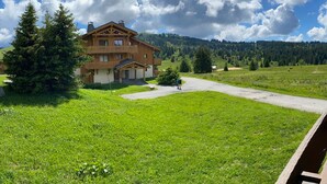 A two-story wooden house with a balcony, surrounded by lush green fields and trees, with a clear sky above. - 3-room Apt Les Saisies, 6 ppl, Pets allowed (Les Saisies)