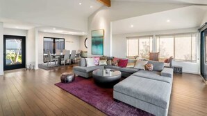 Een ruime woonkamer met een grote hoekbank, een ronde salontafel en een eethoek met stoelen.