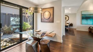 Een modern interieur met een glazen eettafel, een hanglamp en kunstwerken aan de wanden.