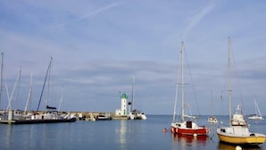 Un puerto deportivo con varios veleros amarrados, un faro y un muelle que se adentra en aguas tranquilas.