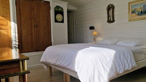 Un dormitorio con una cama, dos mesitas de noche con lámparas, una puerta de madera, un reloj de pared y un cuadro enmarcado.