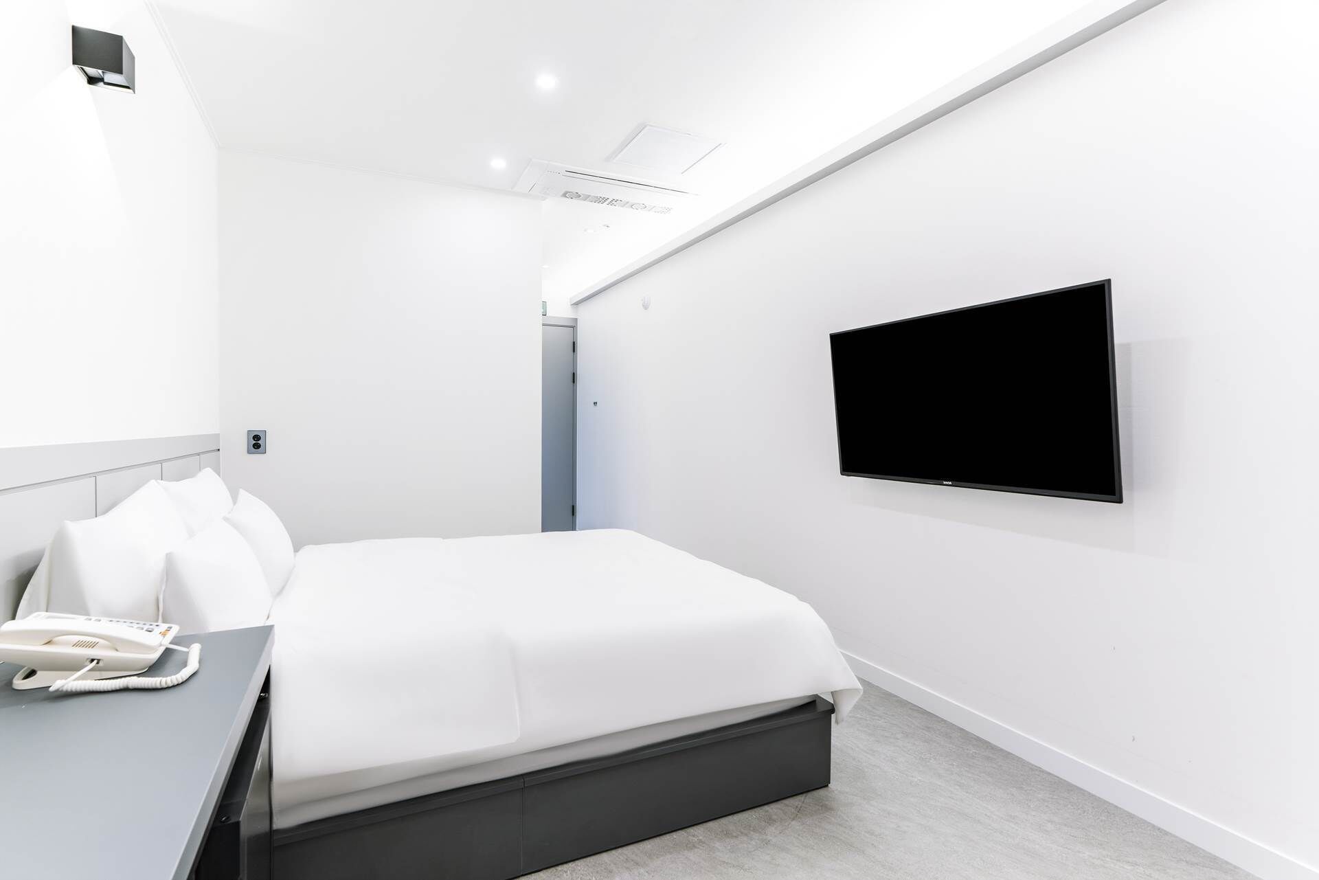 Una habitación de hotel moderna con cama, teléfono en la mesita de noche, televisor de pantalla plana montado en la pared y una puerta que da a otra habitación.
