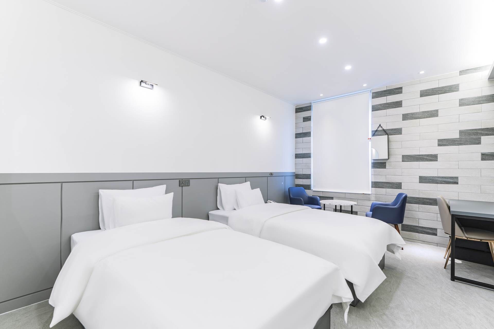 Une chambre d’hôtel avec deux lits, une petite table et un écran de projection.
