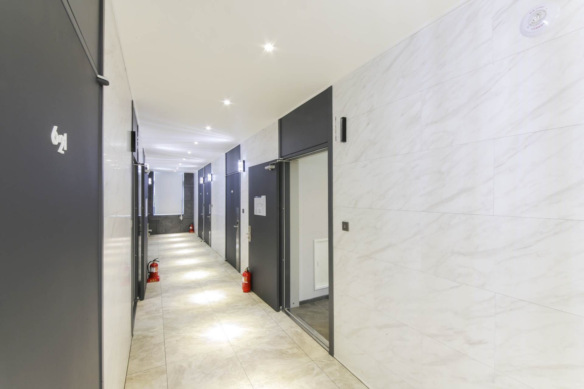 A modern hallway with dark doors, a tiled floor, and a fire extinguisher on the left.