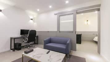 Una habitación de hotel moderna con una mesita de café de mármol, un sofá azul, un escritorio con una computadora y un espejo grande.