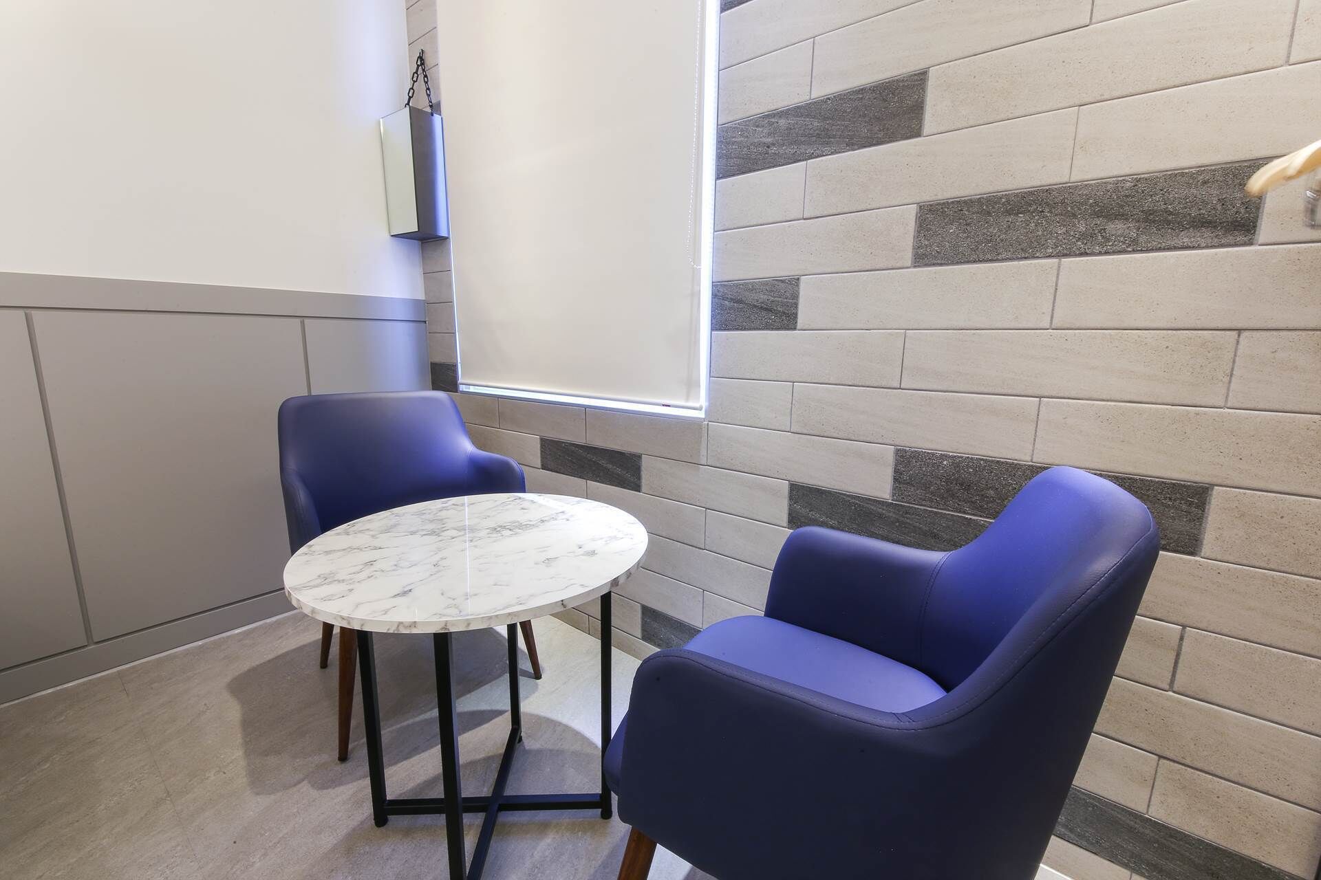 A small room with two blue chairs, a round table, and a tiled wall.
