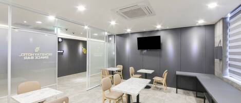 A modern conference room with glass partitions, a flat-screen TV, and multiple tables and chairs.
