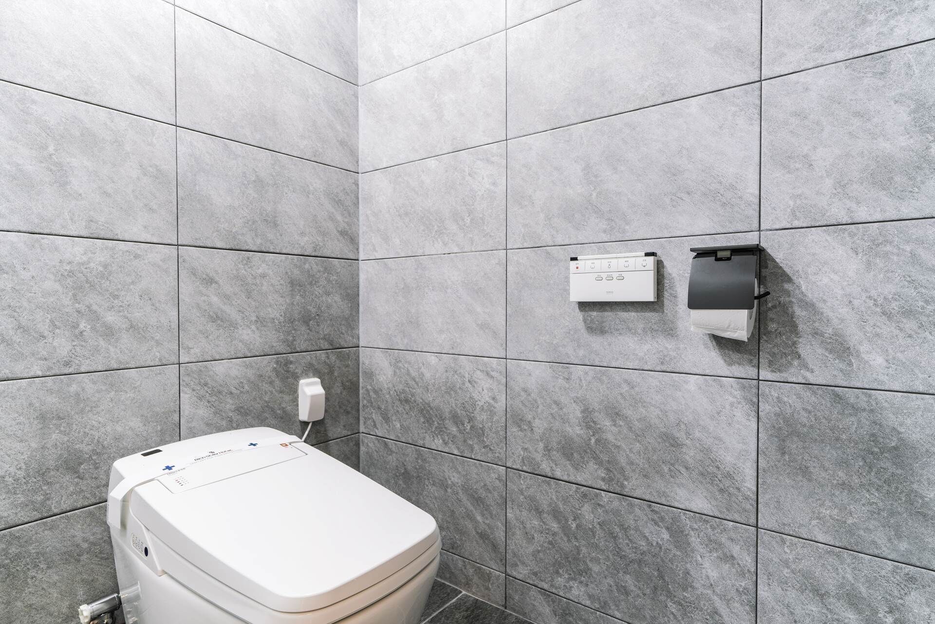 Une salle de bain moderne avec des carreaux gris, des toilettes, un distributeur d’essuie-tout et un distributeur de savon.
