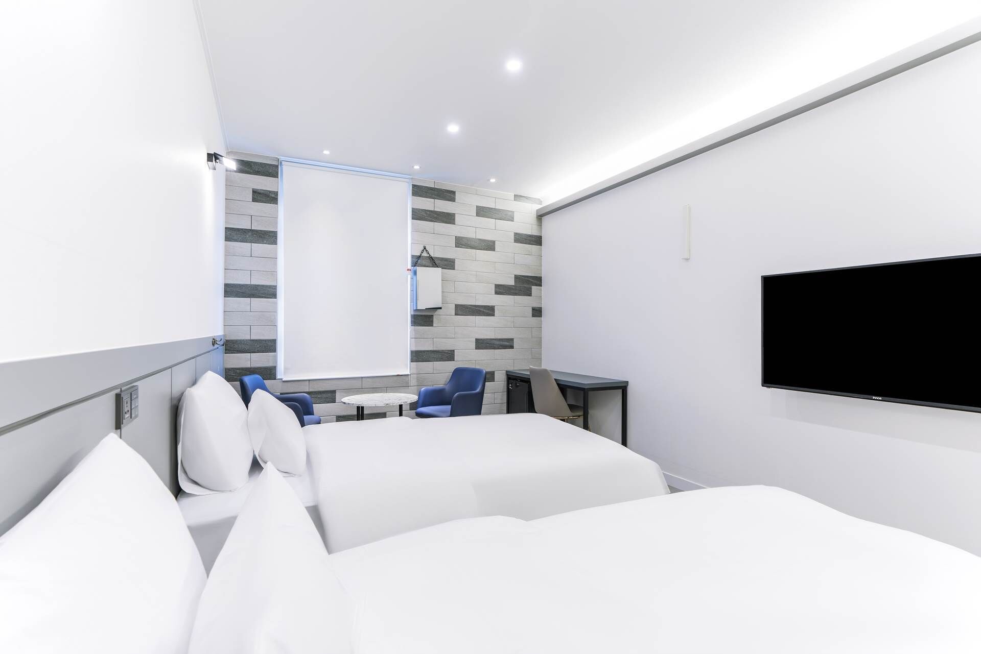 A modern hotel room with two beds, a flat-screen TV, a small round table, and a seating area with chairs.