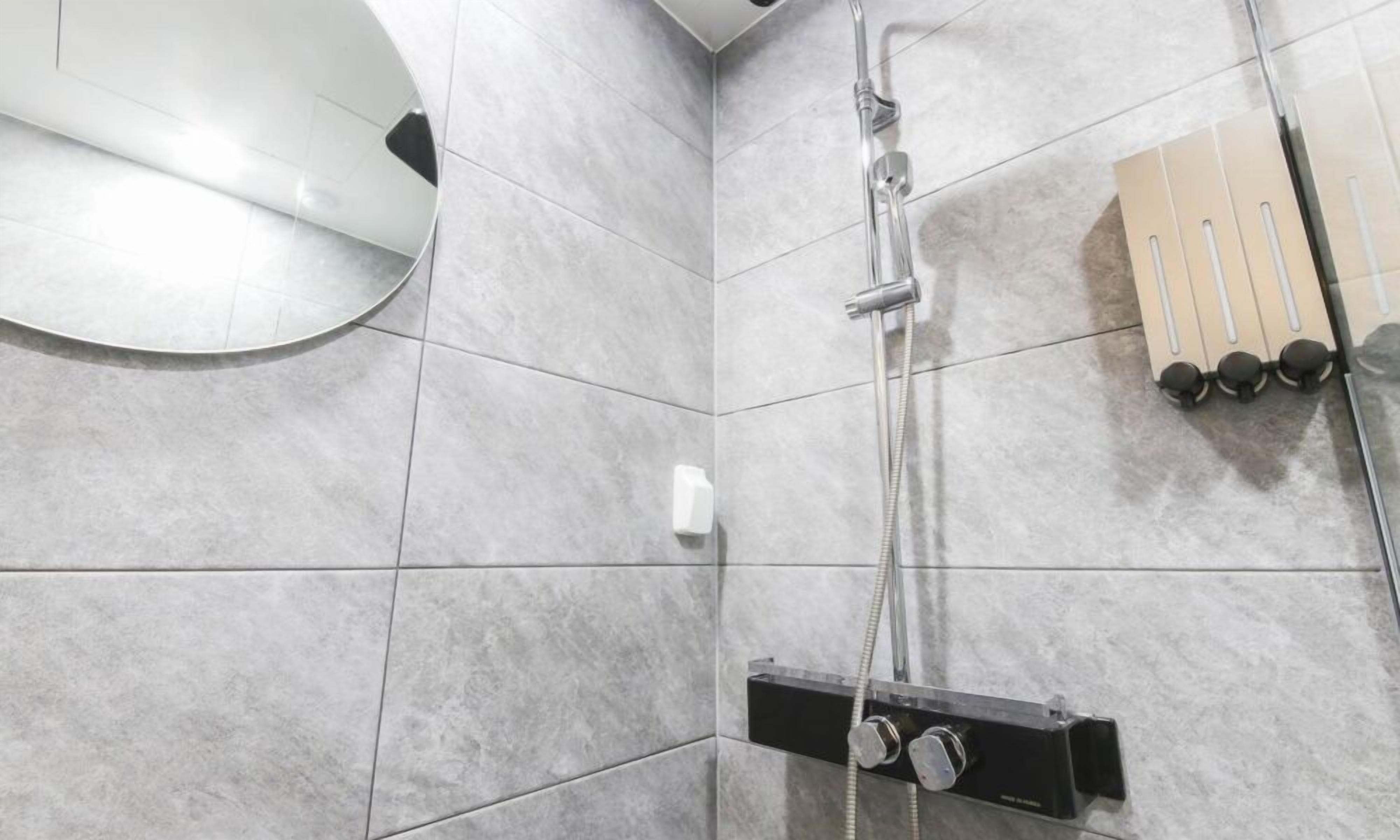 Ein modernes Badezimmer mit grauen Fliesen, einer Handbrause, einem am Wand montierten Wasserhahn und einem Handtuchhalter.