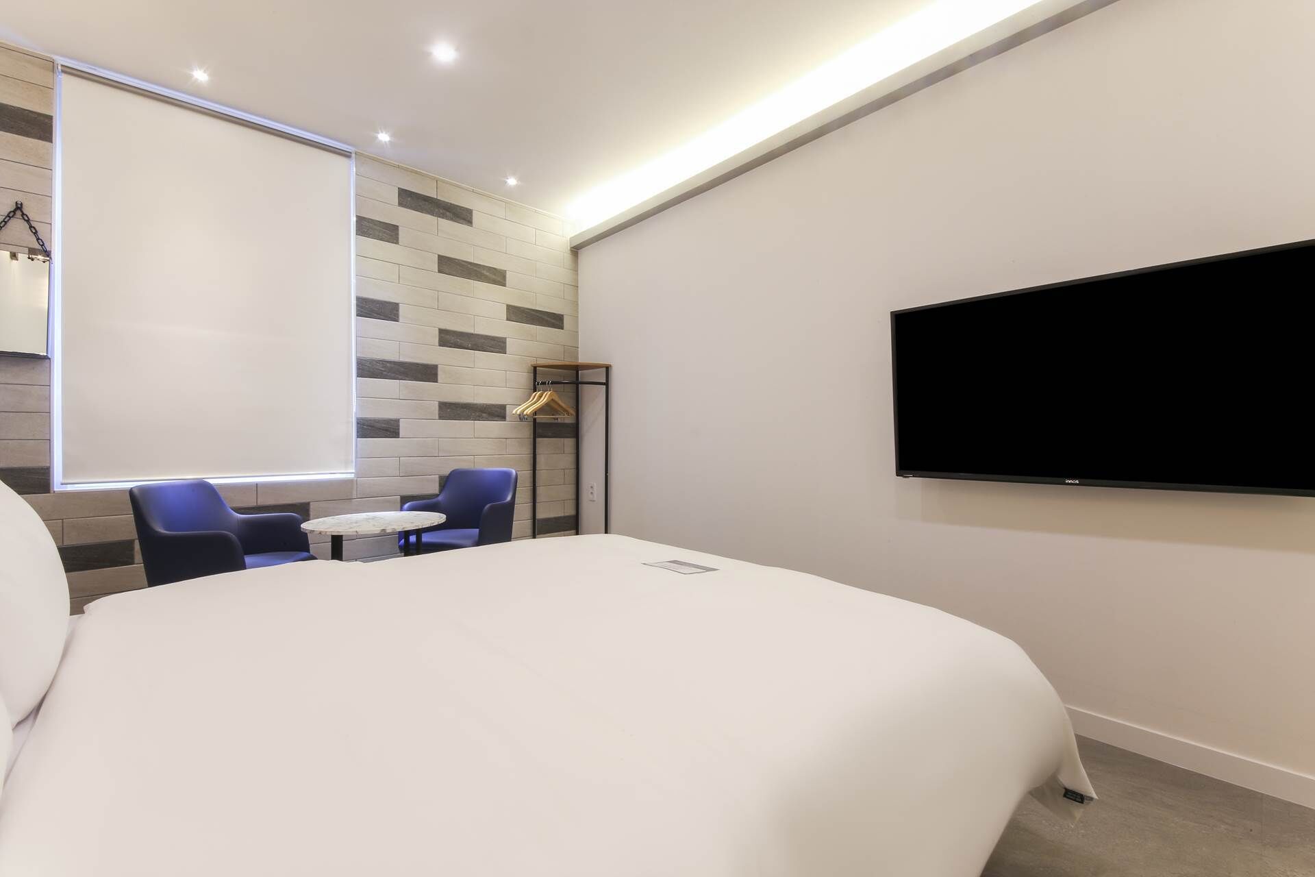 Ein Hotelzimmer mit einem großen Bett, einem an der Wand befestigten Fernseher, einem kleinen Tisch, zwei Stühlen und einem Fenster mit Blick nach außen.