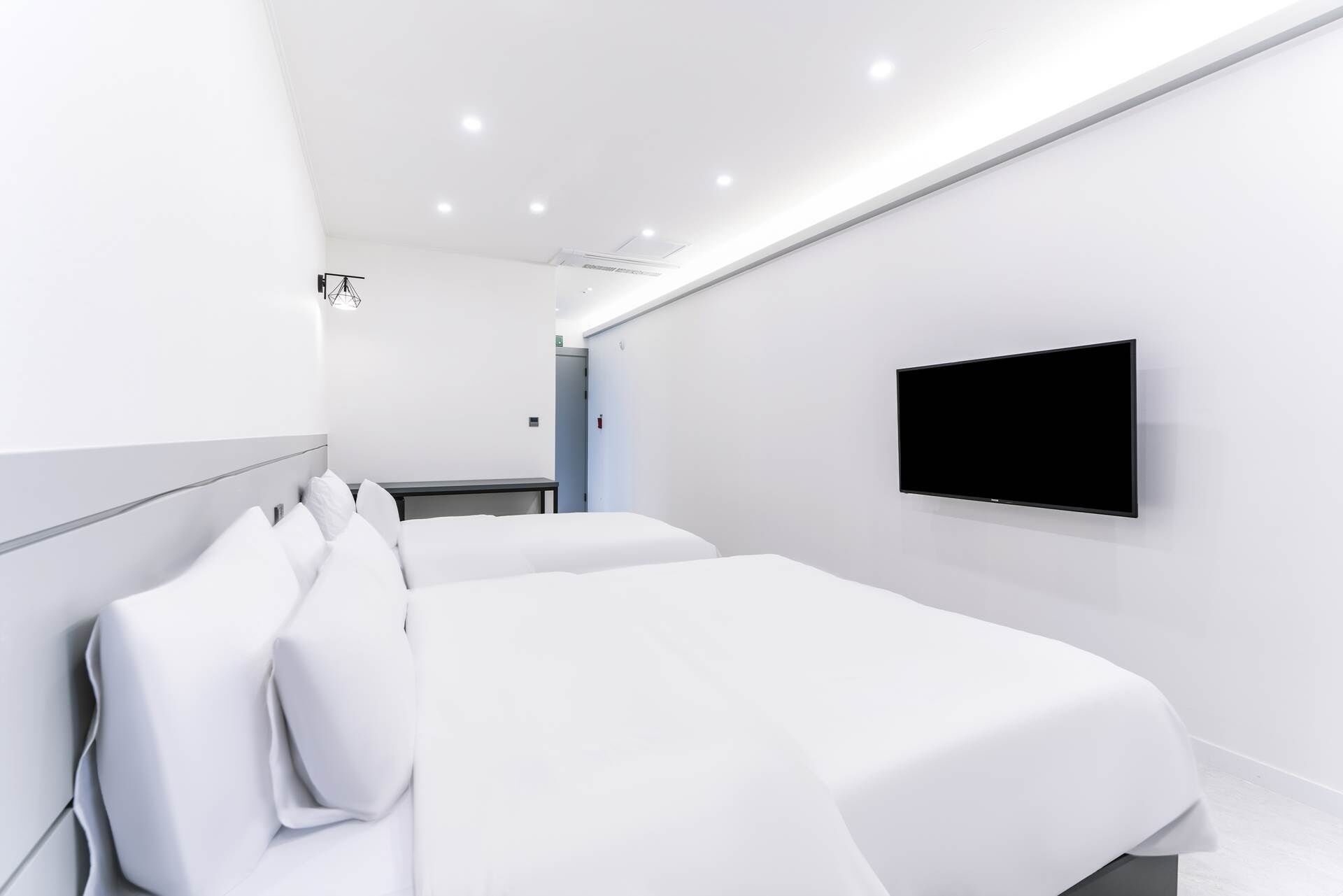 A modern hotel room with two beds, a flat-screen TV mounted on the wall, and a small table.