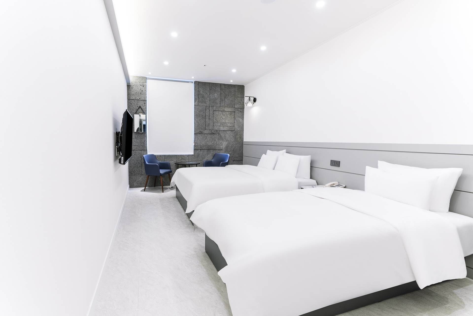 A modern hotel room with two beds, a flat-screen TV mounted on the wall, and a small seating area with two chairs.