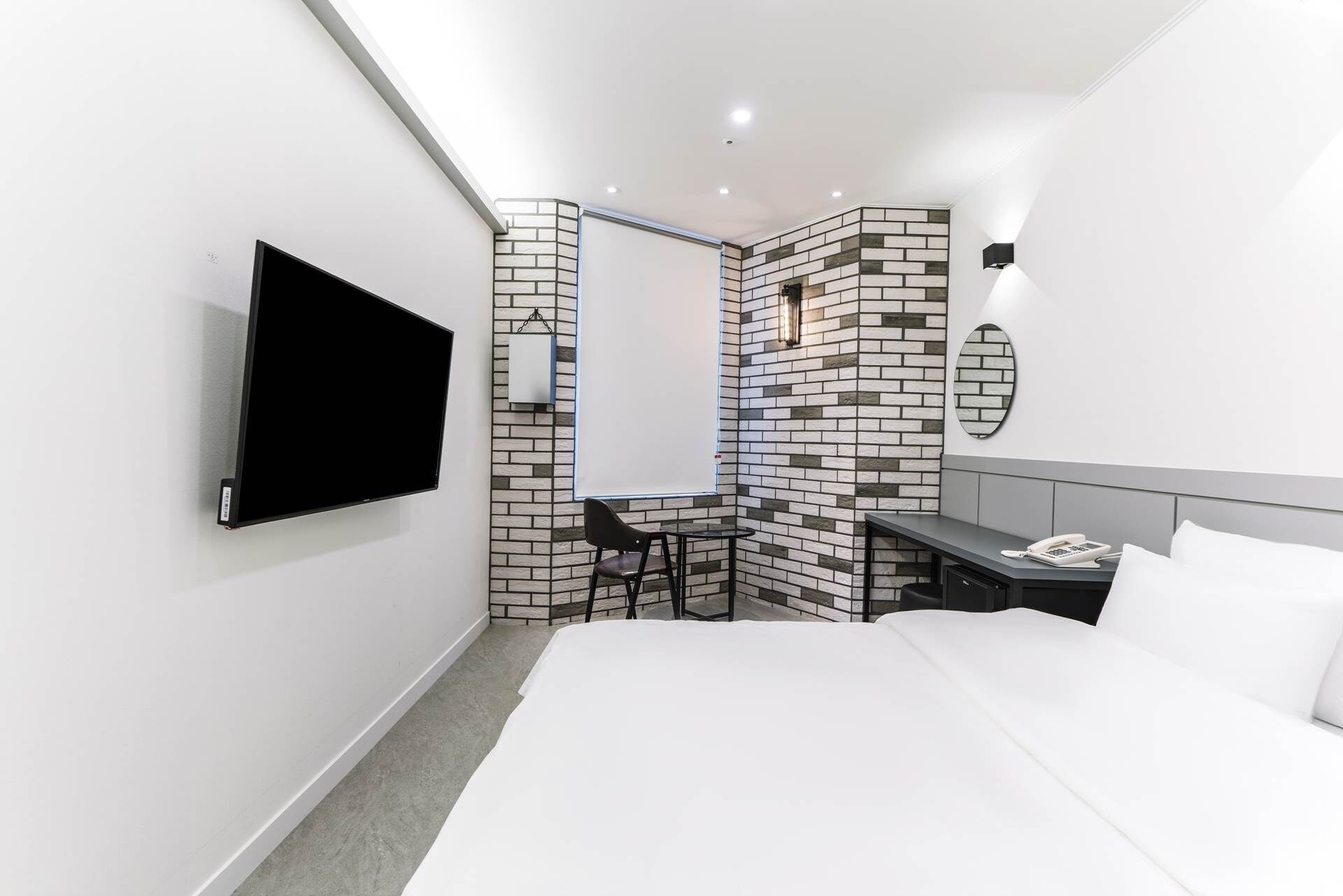 A modern hotel room with a flat-screen TV, a small desk with a chair, a bed, and a wall-mounted phone.