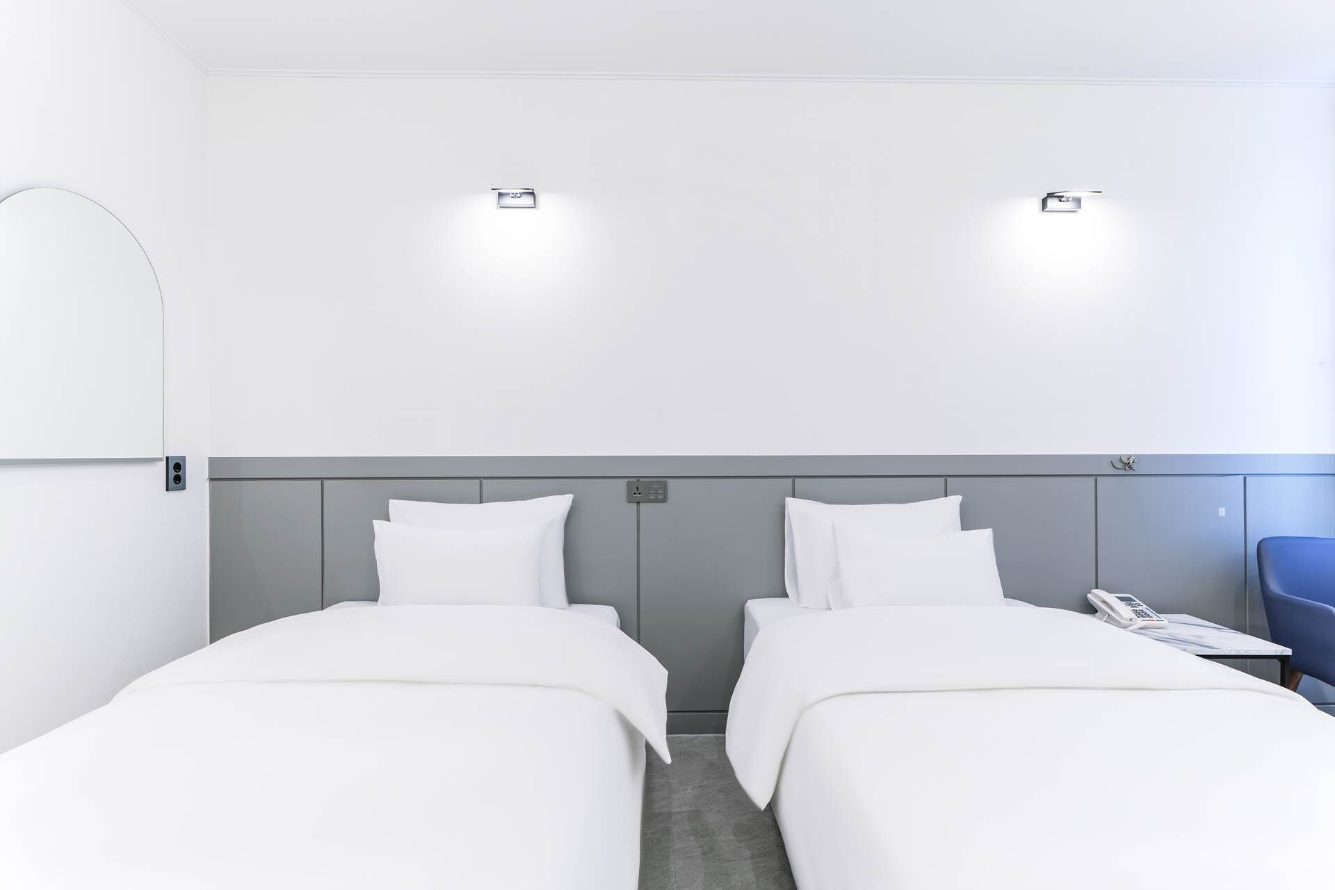 Habitación de hotel con dos camas individuales, una mesita con un teléfono y una silla azul.