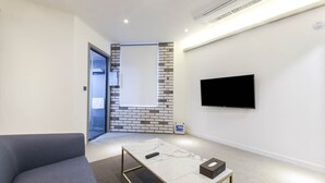 A modern living room with a grey sofa, a marble coffee table, and a flat-screen TV mounted on the wall.