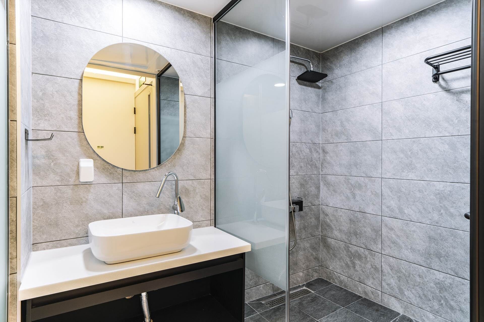 A modern bathroom with a round mirror, a white sink, and a glass-enclosed shower area.
