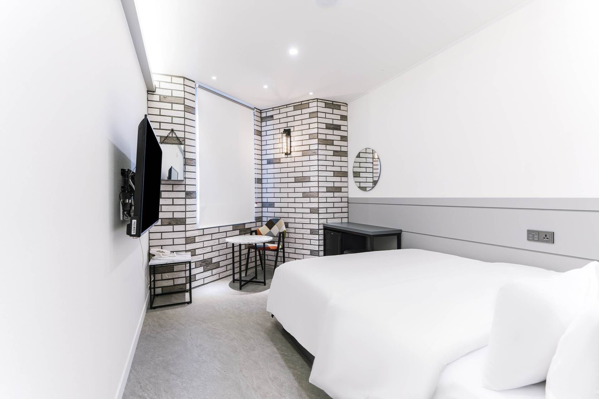 Una habitación de hotel moderna con una cama grande, un escritorio pequeño, una silla, un televisor montado en la pared y un espejo.